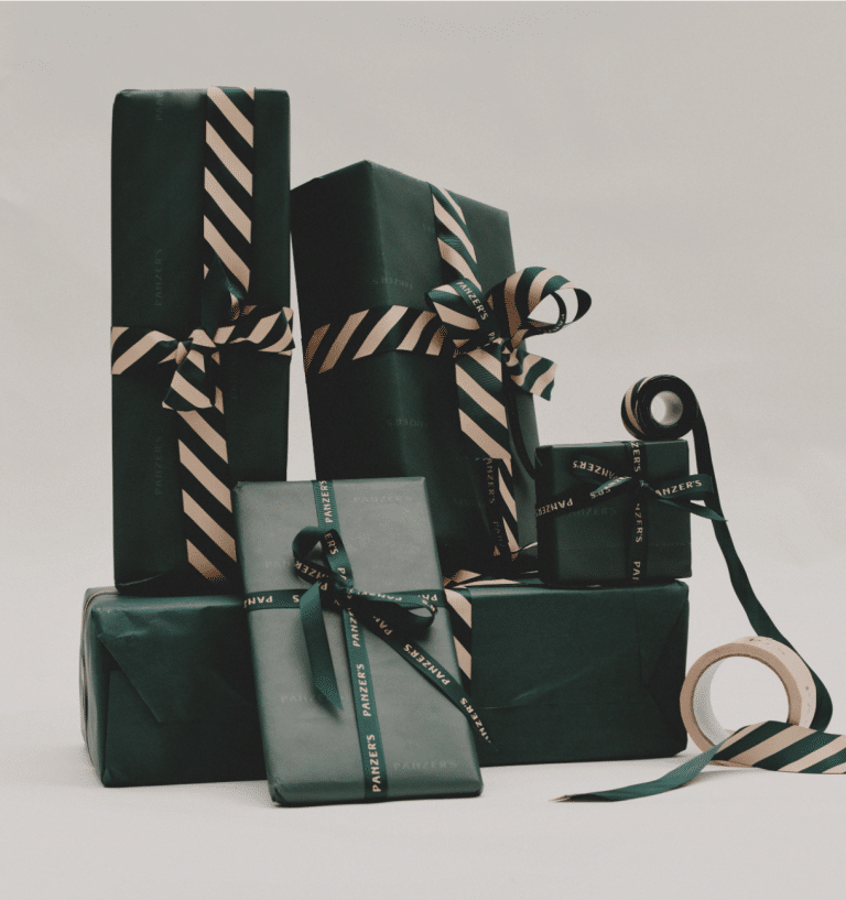 A selection of elegantly wrapped holiday gifts in dark green paper, adorned with striped black and gold ribbon, and branded Panzer's ribbon, set against a minimalist background.