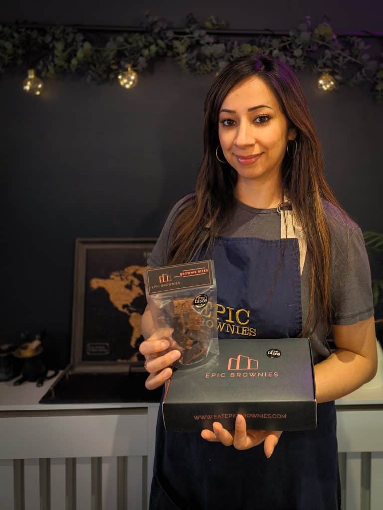 Woman stands in front of dark background holding a box of Epic Brownies