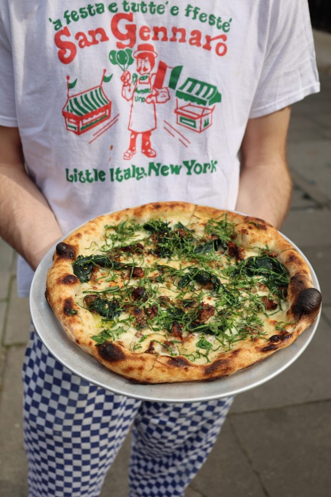 Man holding a plate of pizza with spring toppings like wild garlic and sorrell