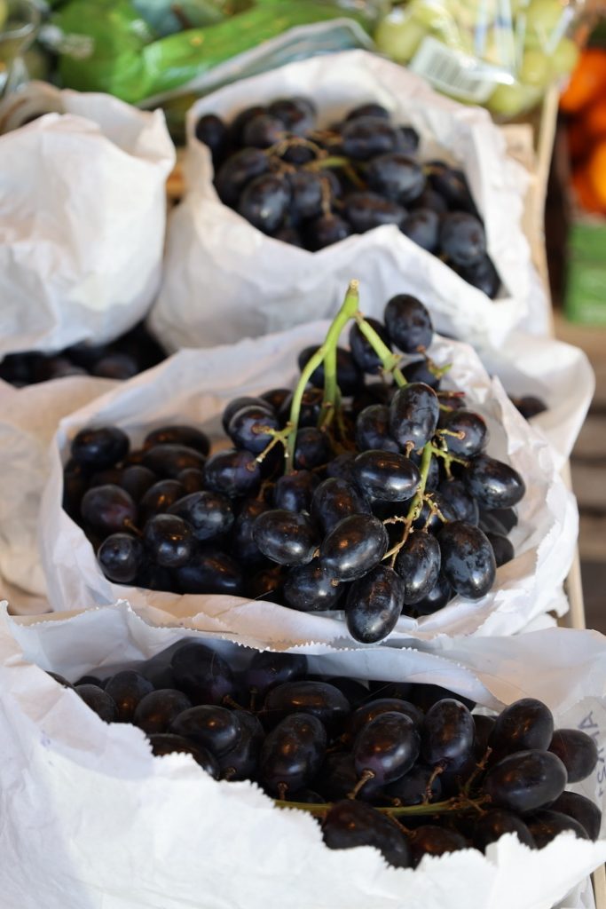 Bunches of dark purple almost black grapes on green stalks wrapped in white paper bags on a display